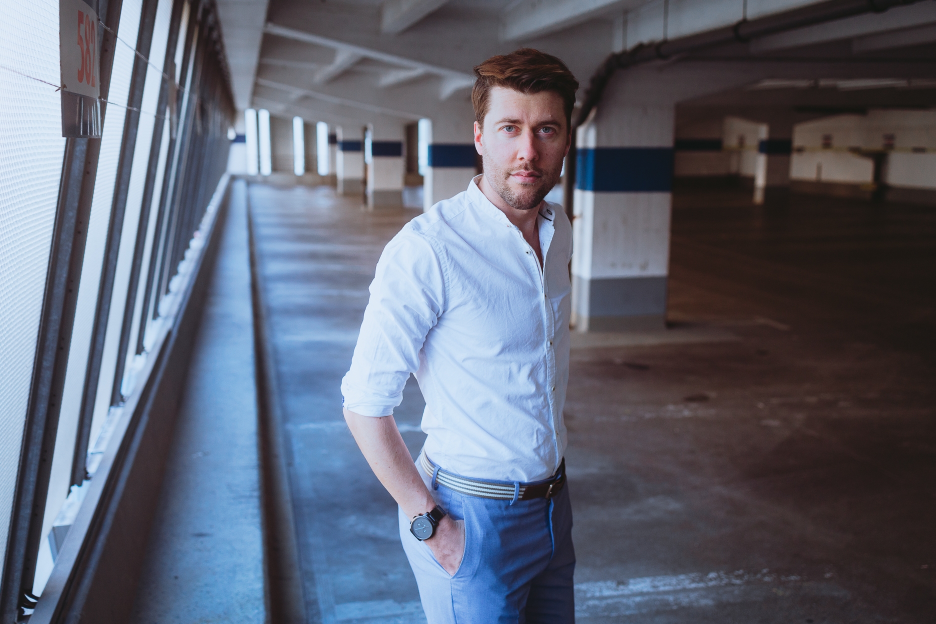 Das etwa 1,80 Meter große, brünette männliche Model Axel posiert in einem Parkhaus in der Abendsonne bei einem Shooting mit dem Münchner Fotograf Daniel Schubert. Das Bild wird auch als Beispiel für Fotografie Kurse oder Portrait Workshops benutzt.