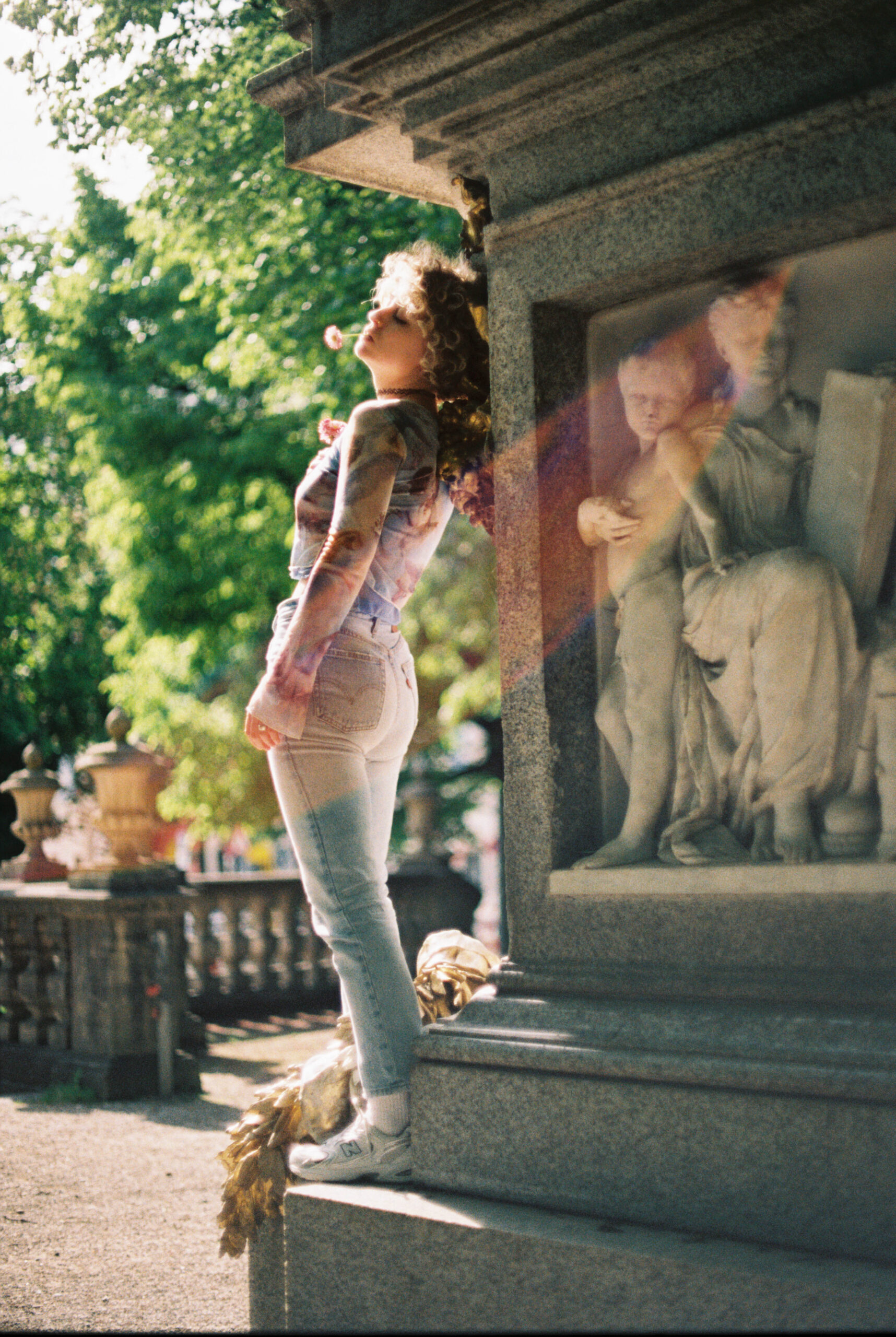 Portrait einer jungen Frau in Jeans in der Gegensonne, neben einer Statue stehend.