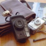 Point and shoot cameras on a table next to a catalog.